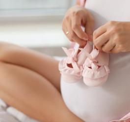 Przyszła mama trzyma na ciążowym brzuchu różowe, niemowlęce buciki.