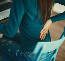 Kobieta siedzi przy biurku, odczuwa ból w dolnym odcinku kręgosłupa.