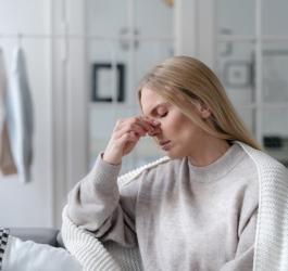 Kobieta trzyma się za nos, może dokuczać jej przeziębienie, jak i zapalenie zatok.