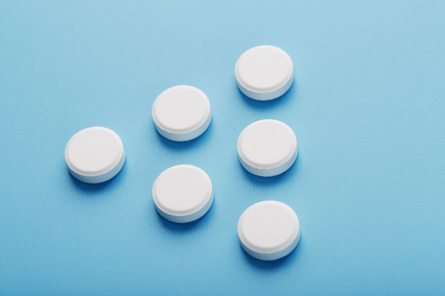 Białe tabletki ułożone w kształt trójkąta na błękitnym tle.