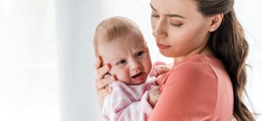 Kobieta trzyma w ramionach niemowlę, które cierpi z powodu męczącego refluksu.