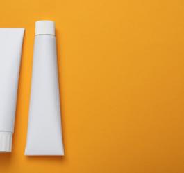 Dwie białe tubki z żelem leczniczym na pomarańczowym tle.