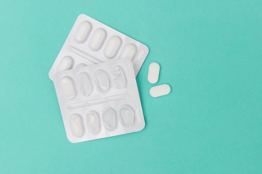 2 blistry tabletek oraz 2 białe tabletki na turkusowym tle.