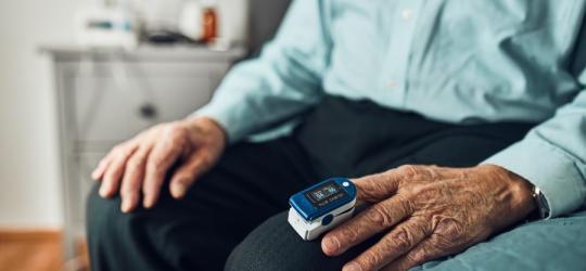 Starszy mężczyzna sprawdza saturację krwi przy pomocy pulsoksymetru.