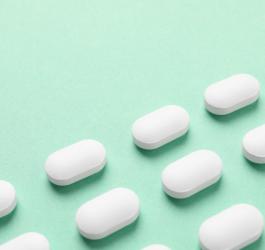 Białe tabletki na seledynowym tle.