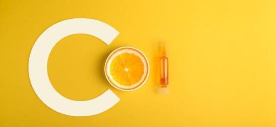 Żółte tło. Litera C, przepołowiona pomarańcza i fiolka serum z witaminą C.