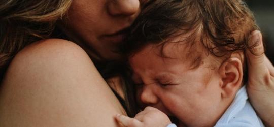 Kobieta trzyma na rękach i tuli płaczące niemowlę.