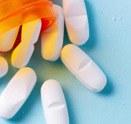 Białe tabletki wysypujące się z pomarańczowego opakowania.