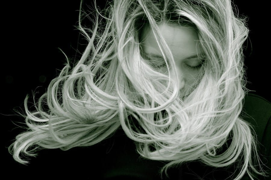 Czarno-białe zdjęcie kobiety o blond włosach, rozwianych przez podmuch wiatru.