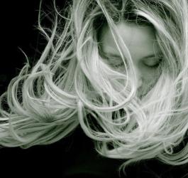 Czarno-białe zdjęcie kobiety o blond włosach, rozwianych przez podmuch wiatru.