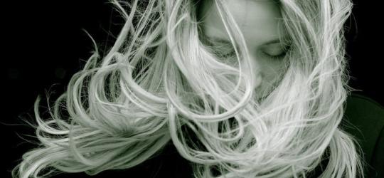 Czarno-białe zdjęcie kobiety o blond włosach, rozwianych przez podmuch wiatru.