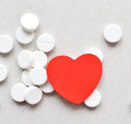 Białe tabletki i wycięte z czerwonego papieru serce na szarym tle.