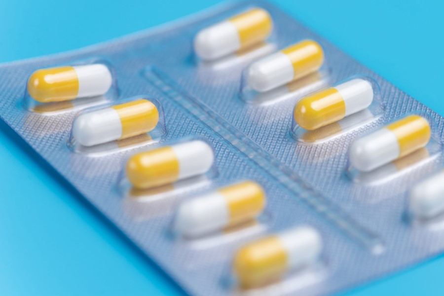 Biał-żółte kapsułki w blistrze na niebieskim tle.