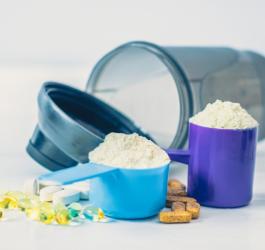 Miarki z odżywką białkową, tabletki i kapsułki z suplementami. W tle shaker do koktajli białkowych.