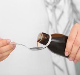 Kobieta nalewa z butelki na łyżeczkę syrop prawoślazowy, stosowany na kaszel.