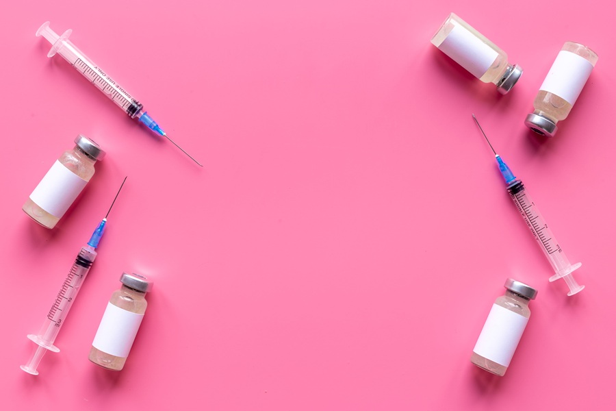 Igły i fiolki ze szczepionkami na różowym tle.
