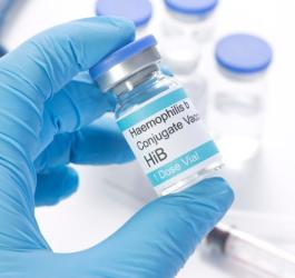 Dłoń w niebieskiej rękawiczce trzyma fiolę ze szczepionką przeciw HiB.