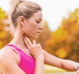 Ubrana na sportowo kobieta przed biegiem w parku mierzy swoje tętno spoczynkowe na tętnicy szyjnej.