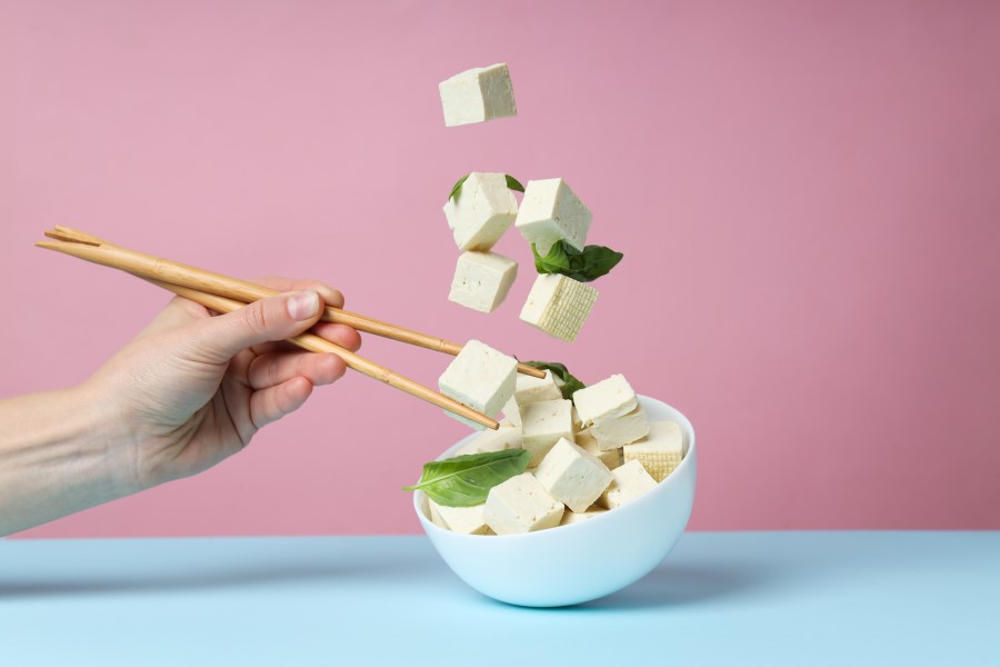 Osoba próbuje pałeczkami chwycić unoszące się w powietrzy kostki tofu.