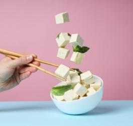 Osoba próbuje pałeczkami chwycić unoszące się w powietrzy kostki tofu.