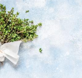 Pęczek tymianu owinięty białym papierem i sznurkiem, leżący na biało-błękitnym tle.