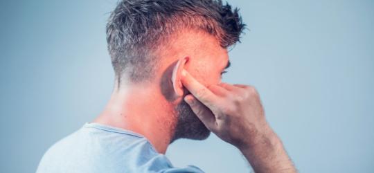 Mężczyzna trzyma się za bolesne ucho. Ból i zaczerwienienie to jedne z objawów ucha pływaka.