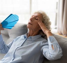 Starsza kobieta wachluje się wachlarzem, jest jej bardzo gorąco i grozi jej udar słoneczny.