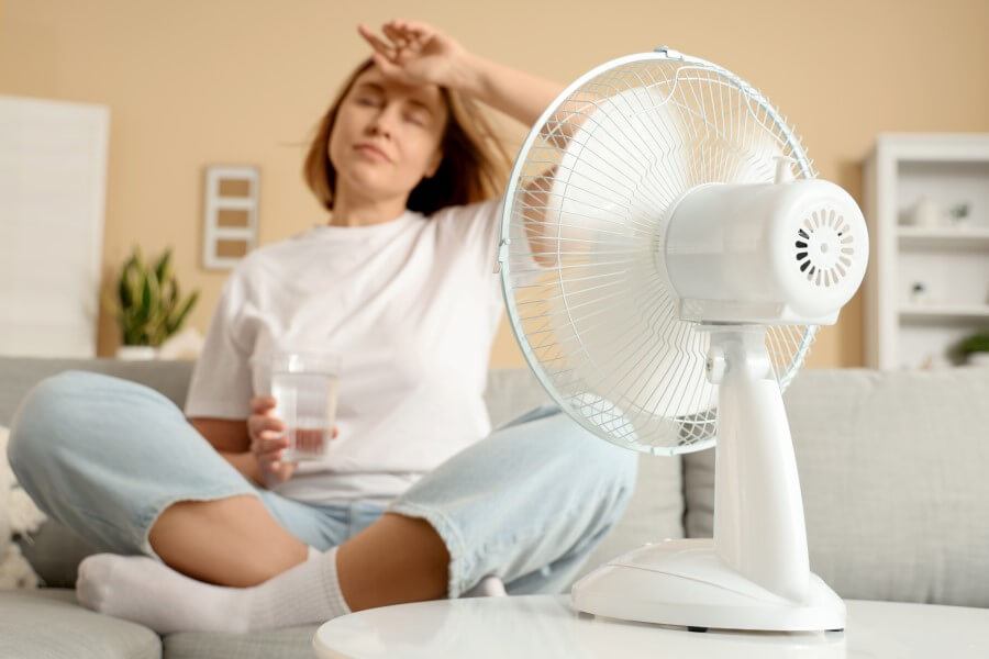 Kobieta schładza się przed wentylatorem, męczą ją uderzenia gorąca.