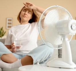 Kobieta schładza się przed wentylatorem, męczą ją uderzenia gorąca.