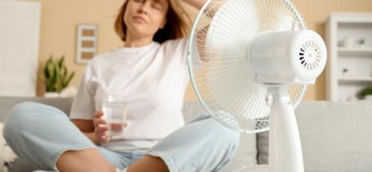 Kobieta schładza się przed wentylatorem, męczą ją uderzenia gorąca.