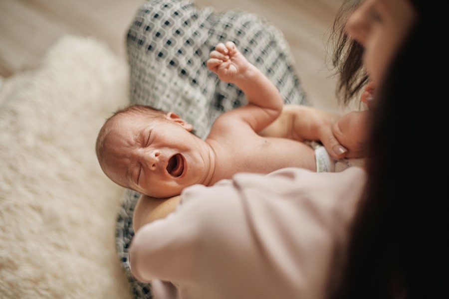 Mama trzyma na rękach noworodka, który płacze.