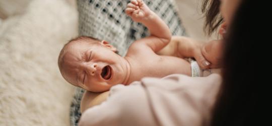 Mama trzyma na rękach noworodka, który płacze.