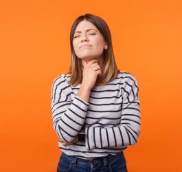 Pomarańczowe tło. Młoda kobieta trzyma się za szyję, czeka ją usunięcie tarczycy.