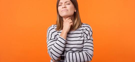 Pomarańczowe tło. Młoda kobieta trzyma się za szyję, czeka ją usunięcie tarczycy.