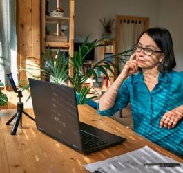 Kobieta w okularach siedzi przy stole, korzysta z laptopa podczas pracy.