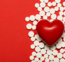 Białe tabletki na czerwonym tle. Na tabletkach leży czerwona figurka serca.