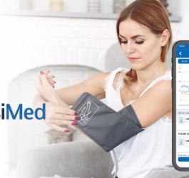 Kobieta mierzy ciśnienie przy pomocy ciśnieniomierza naramiennego. Obok smartfon z aplikacją VisiMed