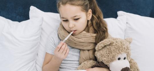 Przeziębiona dziewczynka ma mierzoną temperaturę przy pomocy termometru.