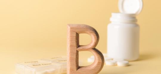 Buteleczka zawierająca tabletki z witaminą B2. Obok drewniana literka B i kasetka na leki.