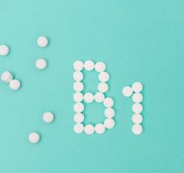 Białe tabletki na niebieskim tle, ułożone w nazwę witaminy B1.