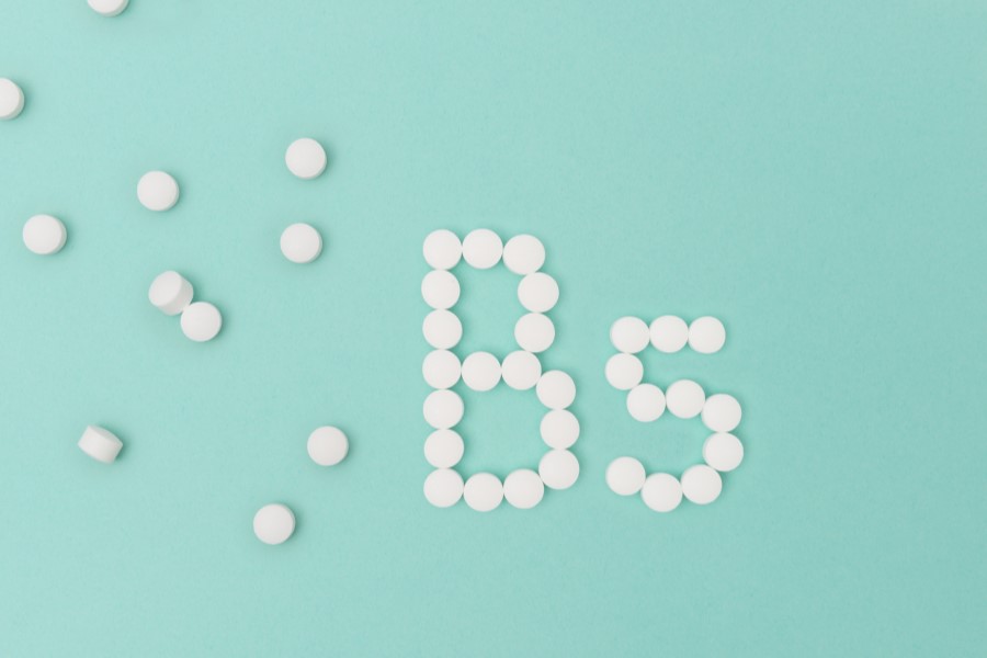 Białe tabletki na seledynowym tle ułożone w napis witamina B5.