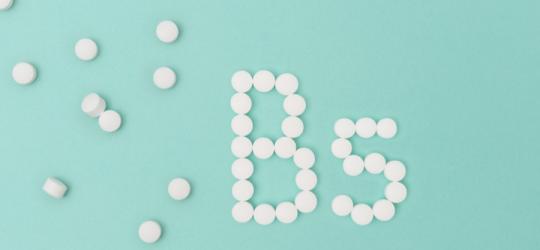 Białe tabletki na seledynowym tle ułożone w napis witamina B5.