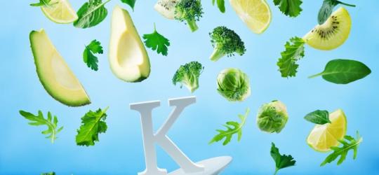 Symbol witaminy K oraz warzywa i owoce będące jej źródłem w diecie.