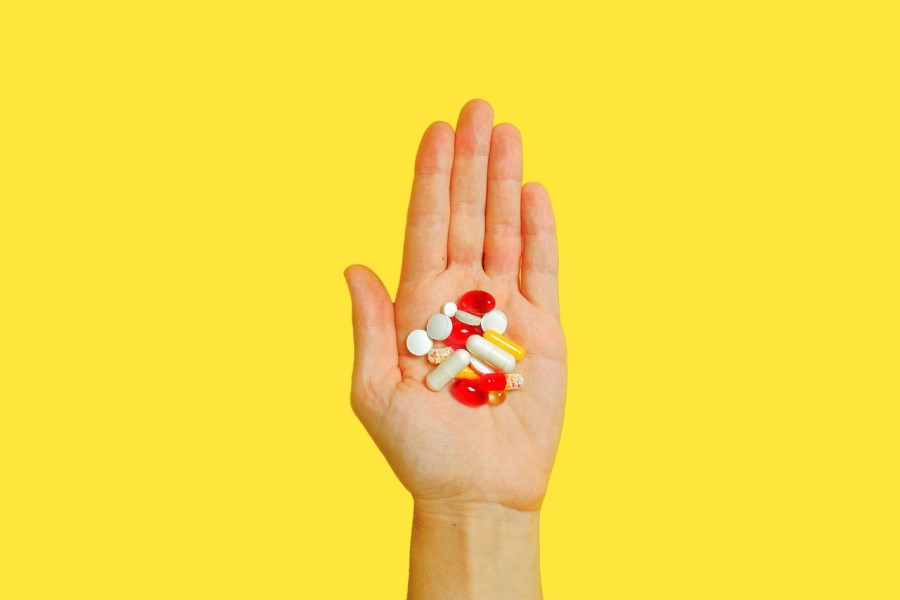 Żółte tło. Osoba trzyma w dłoni rozmaite tabletki kapsułki.