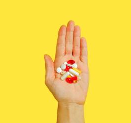 Żółte tło. Osoba trzyma w dłoni rozmaite tabletki kapsułki.