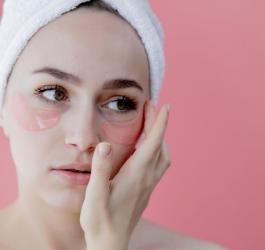 Kobieta po kąpieli, z ręcznikiem na głowie. Nakłada specjalne płatki niwelujące worki pod oczami.