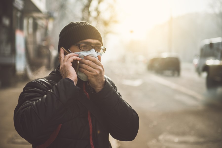 Mężczyzna w zimowych ubraniach rozmawia przez telefon. Ma maseczkę na twarzy chroniącą przed smogiem