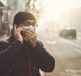 Mężczyzna w zimowych ubraniach rozmawia przez telefon. Ma maseczkę na twarzy chroniącą przed smogiem