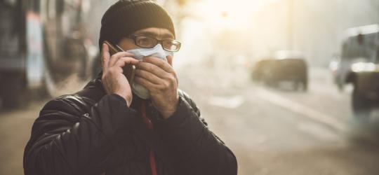 Mężczyzna w zimowych ubraniach rozmawia przez telefon. Ma maseczkę na twarzy chroniącą przed smogiem