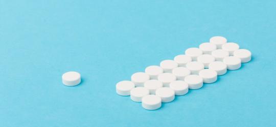Białe tabletki ułożone równo na niebieskim tle.